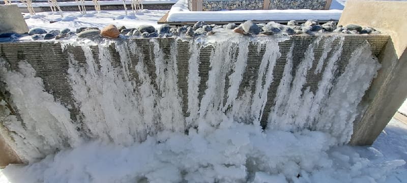 Front view of a water wall covered with long icicles and ice buildup at its base