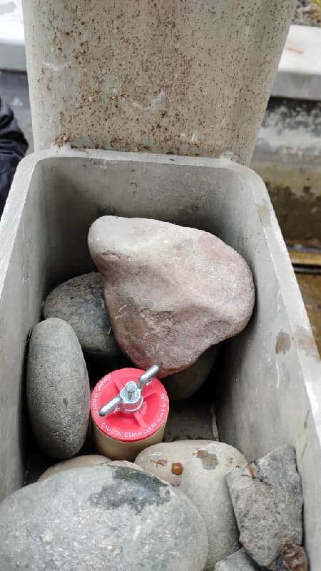 Red mechanical plug installed in a pond plumbing opening among rocks inside a water-feature housing