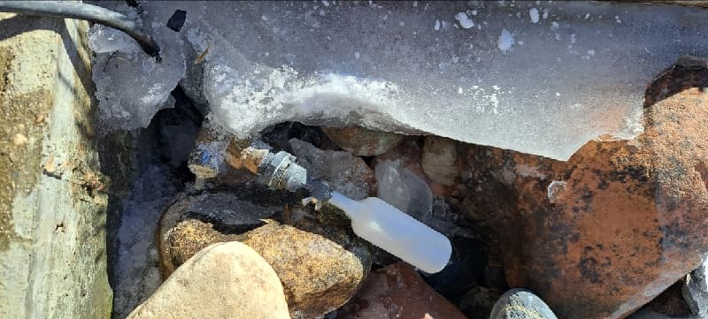 Float valve among rocks beneath a layer of ice in the water feature