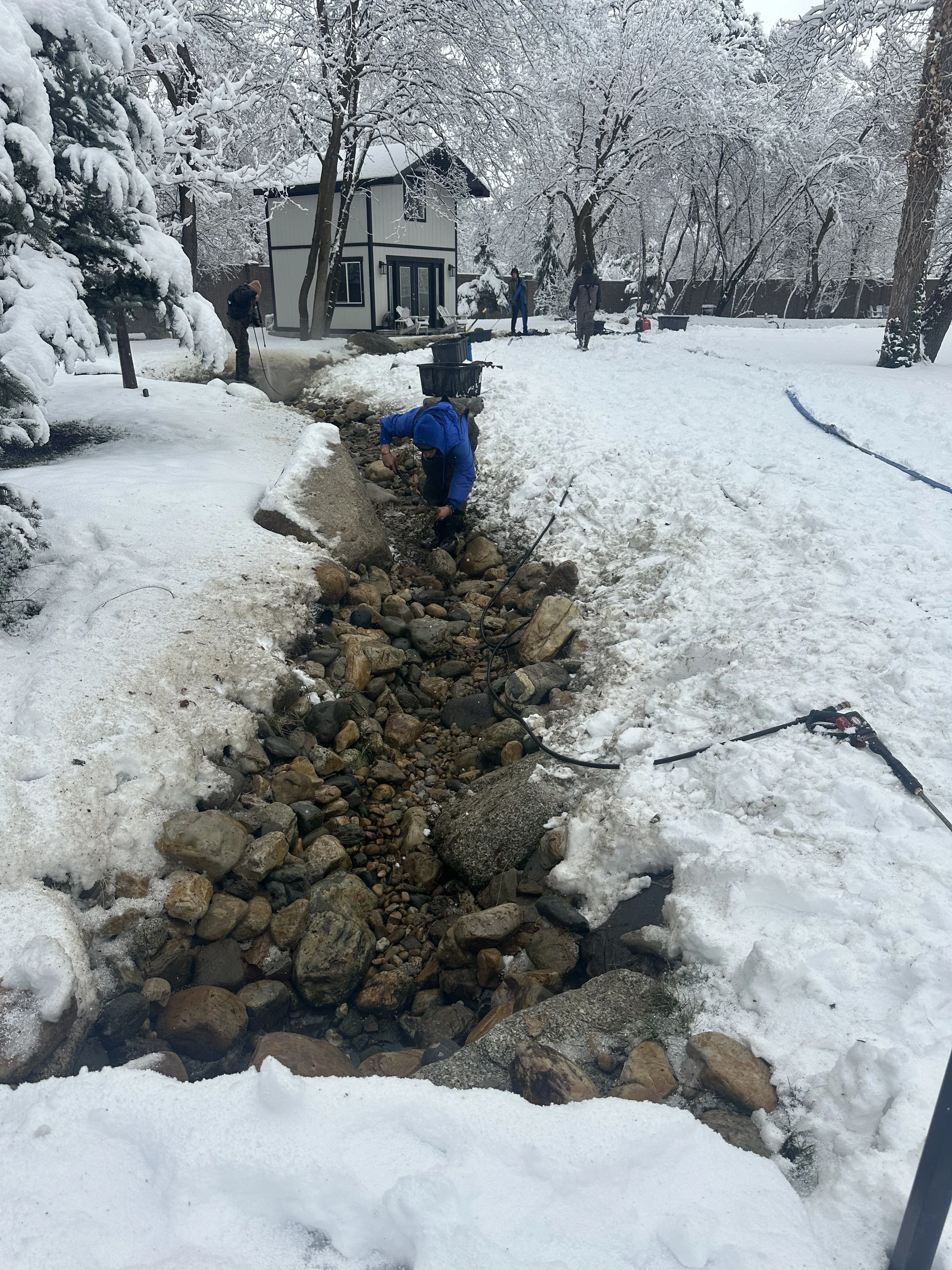 Crew working along a rock-lined water feature in a snow-covered garden