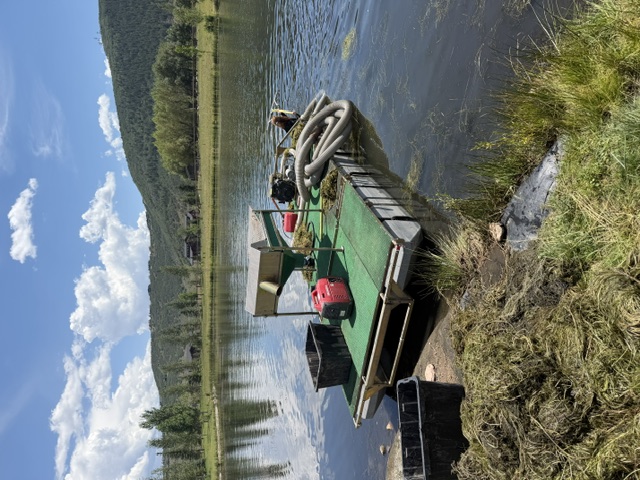 Floating pontoon with screening equipment and hoses at a pond shore