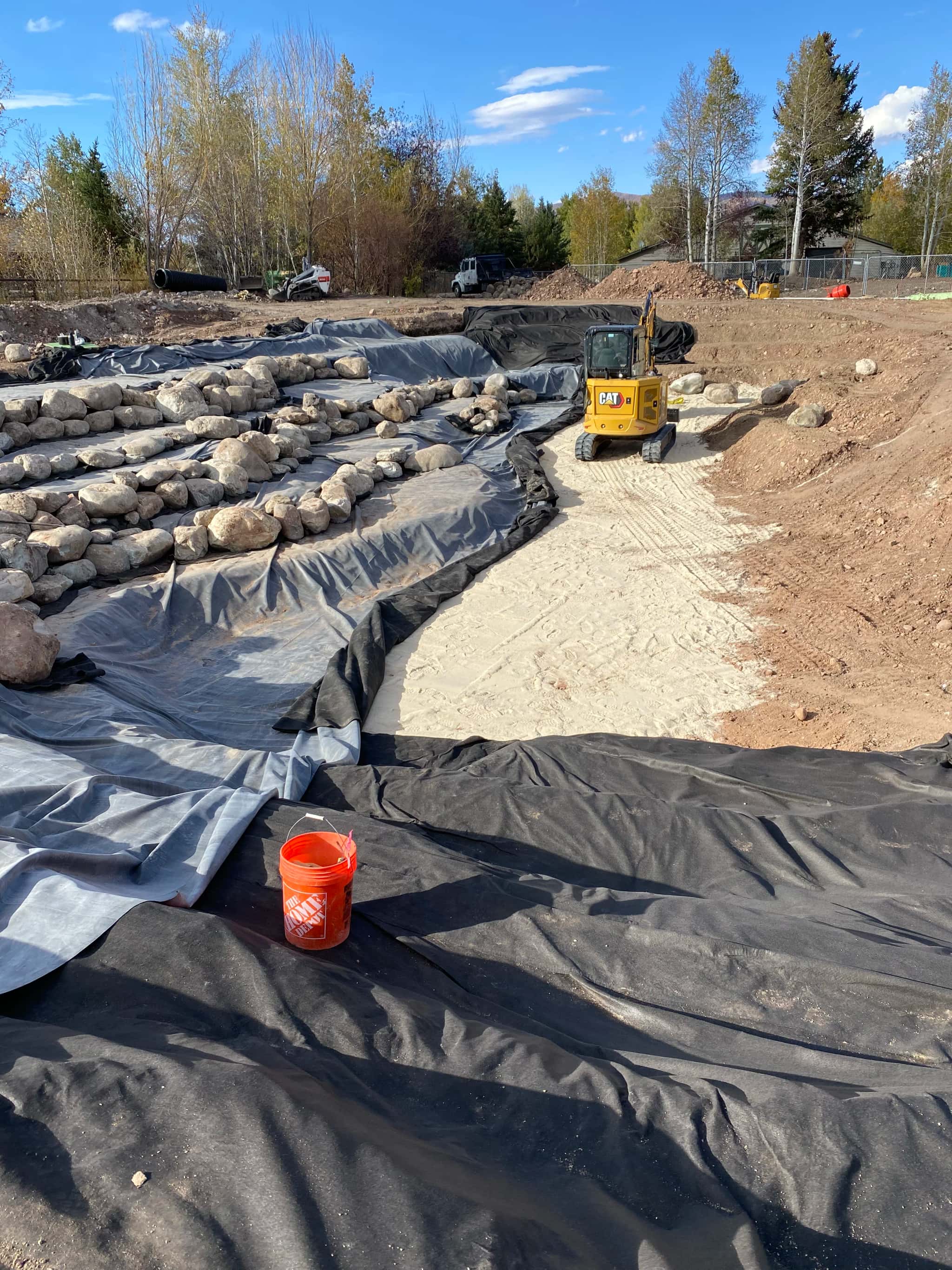 Pond liner and geotextile underlayment installed across wide basin during construction