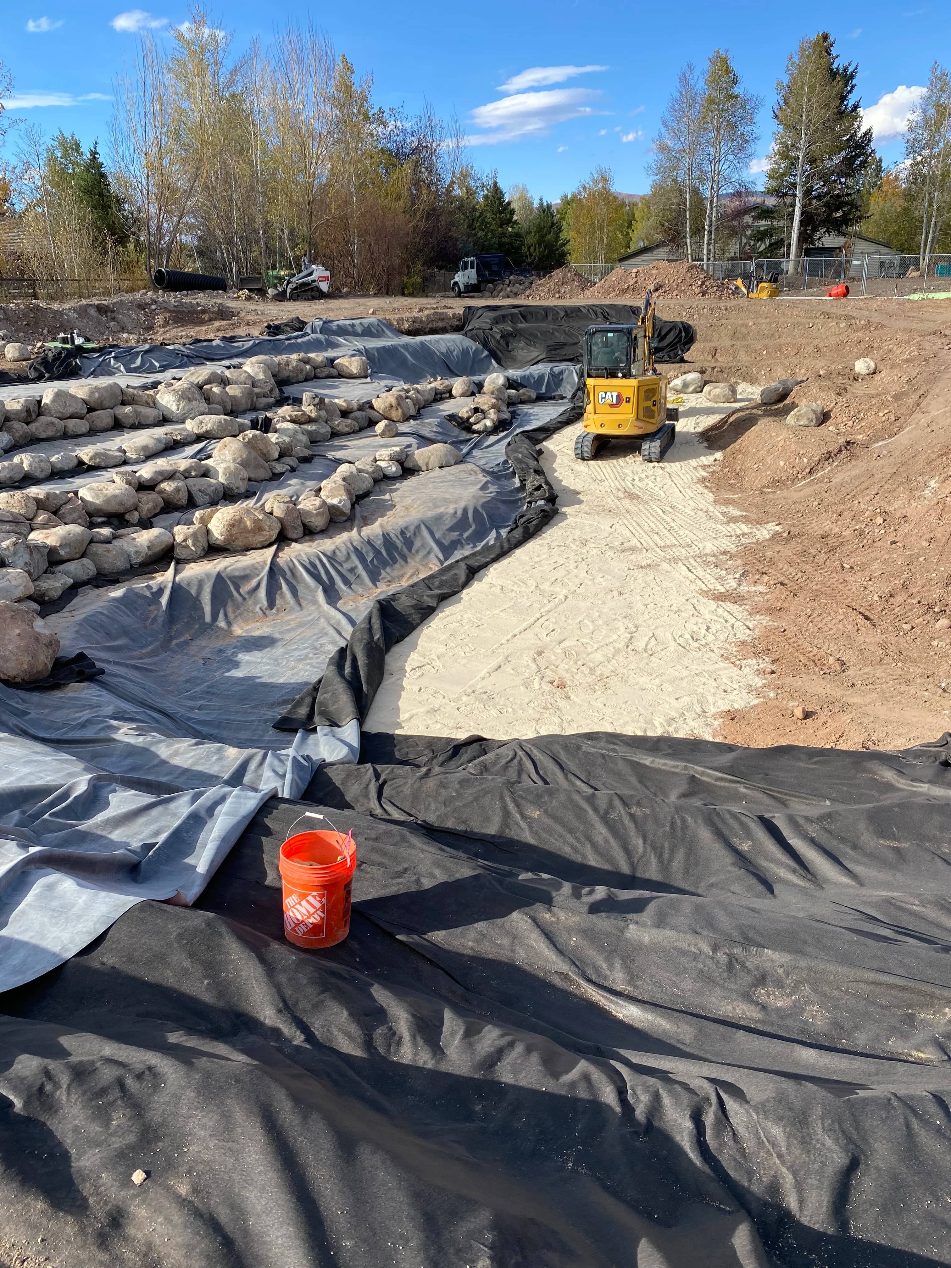 Pond liner and geotextile underlayment installed across wide basin during construction
