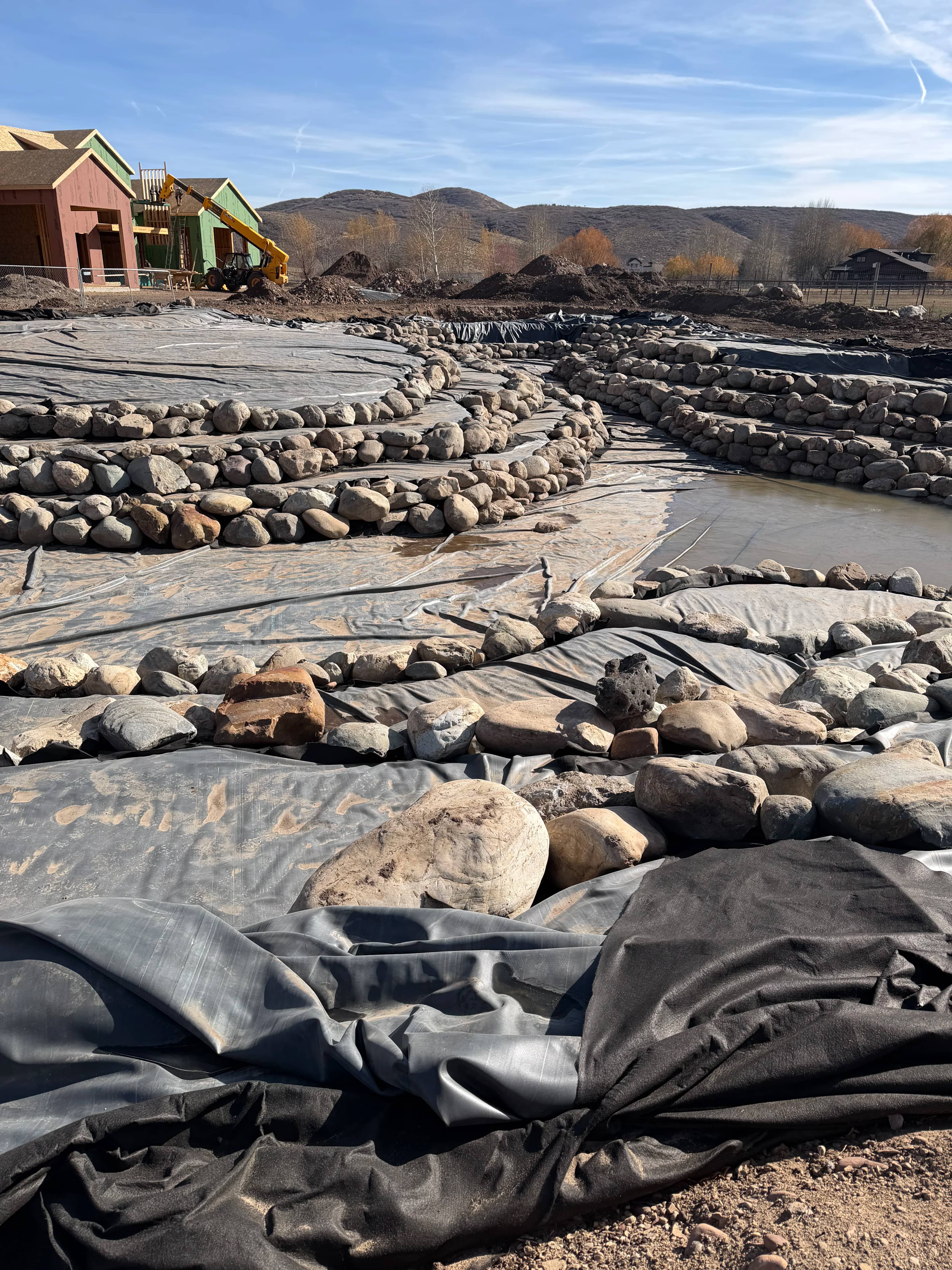 Underlayment and EPDM pond liner laid into excavation with edges left long for proper overlap