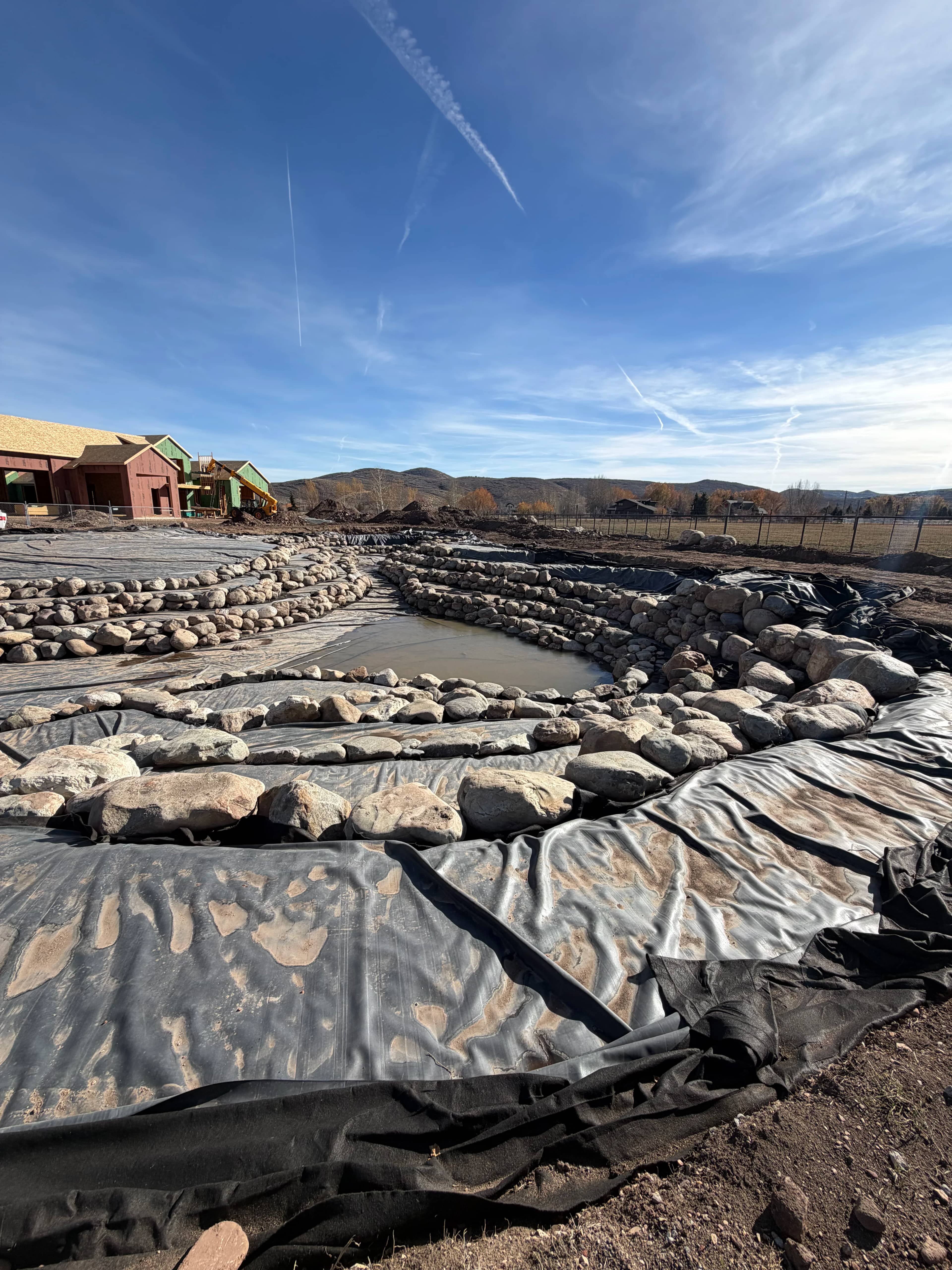 Large pond build with EPDM liner and protective underlayment staged before rockwork
